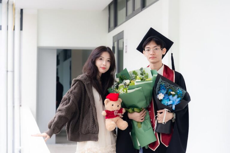 A young graduate holding a bouquet and teddy bear celebrates with a friend.