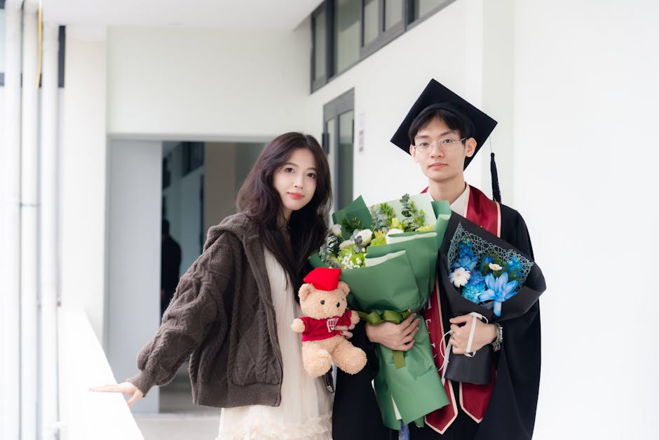 A young graduate holding a bouquet and teddy bear celebrates with a friend.